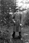 Gustav Andersson i skogen, klädd i rock och keps.