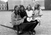 Fyra flickor sitter i en skottkärra på Västra torget i Jönköping. Maj Karlsson (1) född 1916, Majken Karlsson (2) född 1918, Mildred Svensson (3).