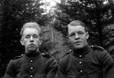 Två män i uniform fotograferade i skogen.
