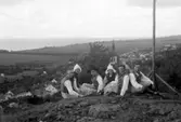Några män och kvinnor klädda i folkdräkt sitter på Grännaberget med utsikt över Gränna och Vättern.