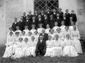 Konfirmandgrupp vid Simtuna kyrka, Uppland, sannolikt 23 juni 1911. I mitten kyrkoherde August Hylander (1852-1935).