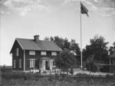 Familj framför hus, ev. Lennartsnäs, Stockholms-Näs socken, ev. 15 juni 1916 (noteringar för EMFWA00025)