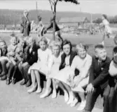 Examensklädda flickor och pojkar sittandes vid gatan. 3:e klass. Tillfällig skollokal på Hagåkersgatan.