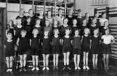 Gruppbild med flickor i gymnastikkläder uppställda i gymnastiksal på Kvarnbyskolan i Mölndal ca 1934.