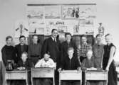 Pojkar sittande i bänkar och stående bakom. Magister Albert Sahlin med elever. På väggen sitter teckningar. Kvarnbyskolan i Mölndal år 1934.