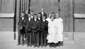 En konfirmandgrupp från Stretereds skolhem fotograferade framför porten till Fässbergs kyrka. Årtal okänt.