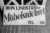 En skylt: John Lindström Möbelsnickeri, Tel 22. Backen 2:10 i Kållered, år 1990.