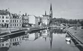 Selångersån. Sjögatan med bebyggelse till vänster på bilden. I bakgrunden Gustav Adolf kyrkan. Vykort.