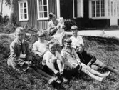 Valdeborg Johansson med hund i famnen tillsammans med sina elever utanför skolan, våren 1934. Text på fotots baksida: 