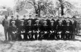 Poliskåren i Mölndal (uniformsklädda med mössor och beväpnade med sabel) samt tre civilklädda män. Samtliga uppställda för gruppfoto i polishusets trädgård, 1952. Personer på bild (ordning ej fastställd): Erik Hernebrink, sittande från vänster, Vahlström, Per Ivar Årgård, Göran Törnqvist, Arne Andersson, Hellqvist, Forsberg, Tony Lindskog, Ernst Gullberg, Arne Barrington, Olof Svensson, Erik Löfgren, Ivar Jansson, Åke Wägnegård, Arne Swärd, Eric W. Karlsson, Harry Wennerberg, Åke Kristiansson, Rolf Lehnberg, Carl Johansson, Nils Rasmusson, Gustav Adolf Bergström. Forsåkersgatan i bakgrunden.