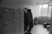 Dokumentation av Sagåsens flyktingförläggning 1992. Ett skåp med flera boxar där det sitter nycklar i för att kunna låsa in personliga saker till de olika rummen. Man ser också en klädhängare med kläder, några kartonger samt ett stängt fönster i bakgrunden.
