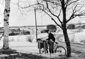 Lantbrevbärare, postiljon Erik Bergman (cykelåkande) i
Delsbo.  April 1956.

Brevbäringsturen är 2 ½ mil lång och omfattar nästan 300 hushåll. Postväskan väger ofta 30-40 kg.