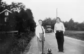 Arvid och Gustav med hund utanför sitt hem Antons, 1930-talet. En tidstypisk bil kommer bakom.