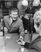 Flyktinghjälpen resulterade i samlingsrekord - 13 milj kr betalades
in på 150 minuter. (Se Tidningen PS nr 6/1967 och 4B/67 samt Postens
Kundtidning nr 2/1967). Foto 16/4 1967. Långa köer vid
postexpeditionen Danderyd 2, Nora torg 4. Thore Skogman lämnar en
kund ett kvitto på inbetalt bidrag.