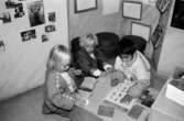 Tre barn sitter på golvet och leker med föremål från museet. Utställningsvernissage av och om Katrinebergs daghem på Mölndals museum 1993-09-10.