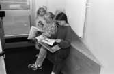 Tre flickor står lutade mot en entrévägg och läser tidningar. Utställningsvernissage av och om Katrinebergs daghem på Mölndals museum 1993-09-10.