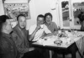 Helmer Garthman, Carl-Gustav, Bror Eriksson och Doris Eriksson sitter i köket på Lerbrännargatan 1F, 1960-tal. Obs! man ser bussgaragen genom fönstret. Skänkt av sonen Alf Garthman.