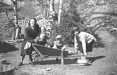 Besök hos Margit och Folke Larsson i Toltorpsdalen i början av 1950-talet. Från vänster: Hilma Johansson med dottern Britt som sitter i skottkärran tillsammans med Alf Garthman och Per-Olof Larsson. Till höger: Margit Larsson f. Karlsson (moster till Alf Garthman).
