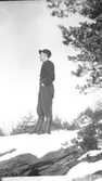 Helmer Garthman, iklädd keps, tröja, långbyxor och stövlar, står på en snötäckt bergsknalle och tittar på utsikten. Fjärås Bräcka, 1930-tal.