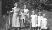 Barnen i familjen Karlsson står vid en cykel på Kvarnfallet 31, år 1936.  Från vänster: Astrid (gift Garthman), Rolf (på cykeln), Margit (gift Larsson), Birgit och Ingrid. Något utav barnen är okänt. Skänkt av sonen Alf Garthman som arbetade under många år på Mölndals stadsmuseum.