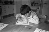 En pojke sitter inomhus vid ett bord och fyller i figurer på ett papper. Katrinebergs daghem, 1992-93.