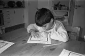 En pojke sitter inomhus vid ett bord och fyller i figurer på ett papper. Katrinebergs daghem, 1992-93.