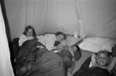 Camping med Katrinebergs daghem. En förskollärare och tre barn ligger nedbäddade bland kuddar och sovsäckar i ett tält.