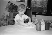 Rick målar med fingerfärg på ett papper som ligger på bordet. Där står tre glasburkar med pinnar i. Lunkentussen, Katrinebergs daghem 1992.