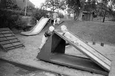 Lekplatsen vid Katrinebergs daghem, 1992. Man ser ett lågt hus att klättra på samt två rutschkanor. Den ena löper utför en backe och den andra som står i en sandlåda.