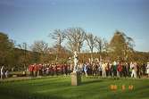 En folksamling som lyssnar på Frälsningsarméns blåsorkester, med en skulptur i förgrunden. Gunnebo slottspark, 1988.