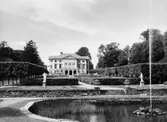 Gunnebo slott och dess södra sida på lite avstånd, 1956. Man ser parken och dammen med en sprutande fontän.