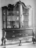Vitrinskåp i mörk färg med inglasad överdel samt tre lådor nertill. Skåpet innehåller diverse olika föremål. Gunnebo slott 1930-tal.