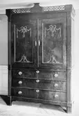 Högt byråskåp i mörk färg med mässingsbeslag, överdel med två stängda luckor och tre lådor nertill. Gunnebo slott 1930-tal.