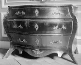 Rokokobyrå av mörkt träslag med mässingsbeslag, tre lådor och utfasat mittenparti. Gunnebo slott 1930-tal.