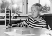 En pojke sitter vid ett bord där det står en kulram. Holtermanska daghemmet 1953.