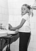 En flicka som sköljer ur en disktrasa vid ett tvättställ. Holtermanska daghemmet 1953.