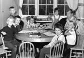 En lärarinna samt en grupp barn som sitter eller står runt ett bord. Holtermanska daghemmet 1953.