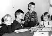 Fyra barn som sitter vid ett bord där det ligger målade teckningar. Holtermanska daghemmet 1953.