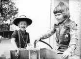 Två cowboy-klädda pojkar som leker med en vattenslang. Holtermanska daghemmet juni 1974.