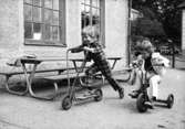 Två pojkar som cyklar på en trehjuling och en sparkcykel. Holtermanska daghemmet juni 1974.
