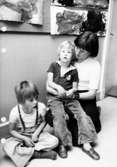 Två barn och en fröken sitter på golvet. Holtermanska daghemmet maj 1975.