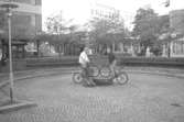 Två killar som poserar på cykel vid skulpturen Albert. Mölndalsbro i dag - ett skolpedagogiskt dokumentationsprojekt på Mölndals museum under oktober 1996. 1996_1079-1097 är gjorda av högstadieelever från Kvarnbyskolan 9C, grupp 4. Se även 1996_0913-0940, gruppbilder på klasserna 1996_1382-1405 samt bilder från den färdiga utställningen 1996_1358-1381.