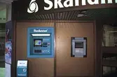 Bankomat utanför Skandinaviska Enskilda Banken på Brogatan/Nygatan. Mölndalsbro i dag - ett skolpedagogiskt dokumentationsprojekt på Mölndals museum under oktober 1996. 1996_1212-1226 är gjorda av högstadieelever från Kvarnbyskolan 9D, grupp 5. Se även 1996_0913-0940.