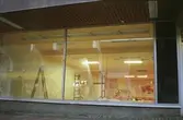 Vy genom en glasruta på en tom butikslokal som renoveras. Mölndalsbro i dag - ett skolpedagogiskt dokumentationsprojekt på Mölndals museum under oktober 1996. 1996_1227-1245 är gjorda av högstadieelever från Kvarnbyskolan 9D, grupp 6. Se även 1996_0913-0940.