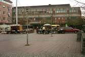 Torghandel på Mölndals torg. Brogatan (kvarteret Kungsfisken 4) i bakgrunden. Mölndalsbro i dag - ett skolpedagogiskt dokumentationsprojekt på Mölndals museum under oktober 1996. 1996_1320-1337 är gjorda av högstadieelever från Åbyskolan 8A, grupp 5. Se även 1996_0913-0940, gruppbilder på klasserna 1996_1382-1405 och bilder från den färdiga utställningen 1996_1358-1381.