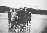 Sex skridskoklädda personer befinner sig på en frusen sjö (troligtvis Färåstjärn/Bergsjön) i Kållered, 1920-tal. En utav dem sitter på en skrinda.