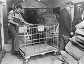 Pkp 313. I Långsele tas en container ombord. Ingemar Holm låser
fast sidostyckena. Containern lastas under vägen med post till Umeå
trans för lossning i Vännäs. T.h. byrådirektör Gösta Sundman från
poststyrelsens driftbyrå. Byrådirektör Sundman premiäråkte
tillsammans med Åke Ström från Järnvägsposten i Mellersta Distriktet.
De har båda tillhört arbetsgruppen som kommit med förslag till
inredning av den nya vagnen.