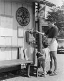 Sommargäst med dotter vid kiosken i Dalarö brygga,  postar ett girokuvert, 1961. Bilden är arrangerad.