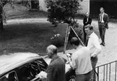 Inspelning i Arboga där försök med utökad lantbrevbäringsservice
på-gick. Filmfotograf Norberg mäter exponeringen. Regissör Johansson
ser på. I bakgrunden postmästare Lennart Ljungstedt (t.v.) och
byrådirektör Eberhard Löfvendahl, poststyrelsen.