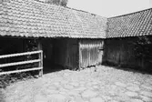 En stensatt gårdsplan med ekonomibyggnader runt omkring.
Högen 2:1/2:2 i Kållered, 1992-06-30.